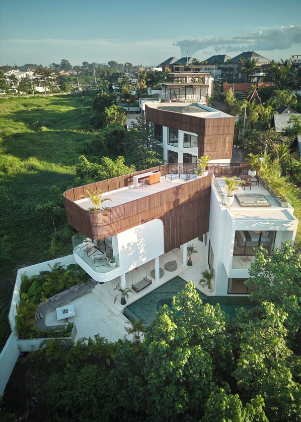 A modern house with a rooftop terrace, a swimming pool, and lush greenery surrounding it. - The River Villa by BREIG (Munggu)