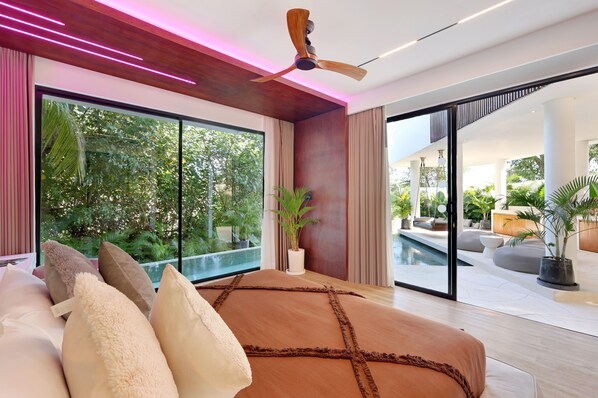 A modern bedroom with a large bed, a ceiling fan, and a view of an outdoor swimming pool. - The River Villa by BREIG (Munggu)