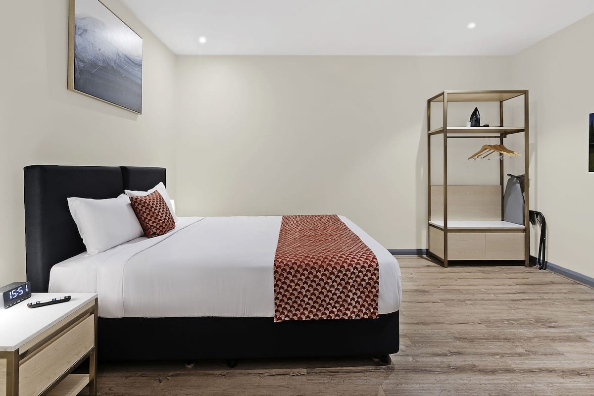 Une chambre d’hôtel moderne équipée d’un lit, d’une table de chevet et d’une armoire intégrée.