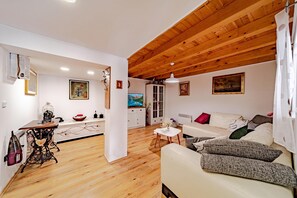 A cozy living room with a wooden ceiling, a sofa with cushions, a television, and a dining area with a table and chairs.