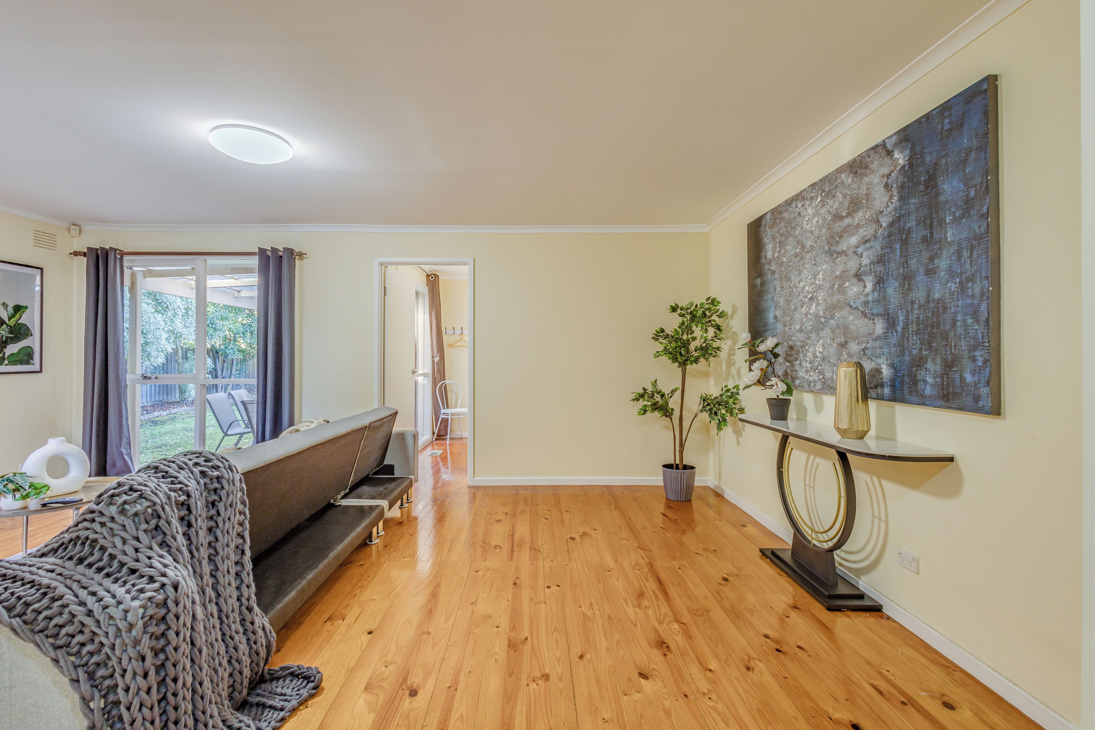 A spacious living room with a wooden floor, a sofa, a coffee table, and a large abstract painting on the wall.