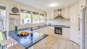 A kitchen with white cabinets, a black stove, and a window with a view of trees. - StayAU Cozy Family Comfort 5BRM Glen (Glen Waverley)