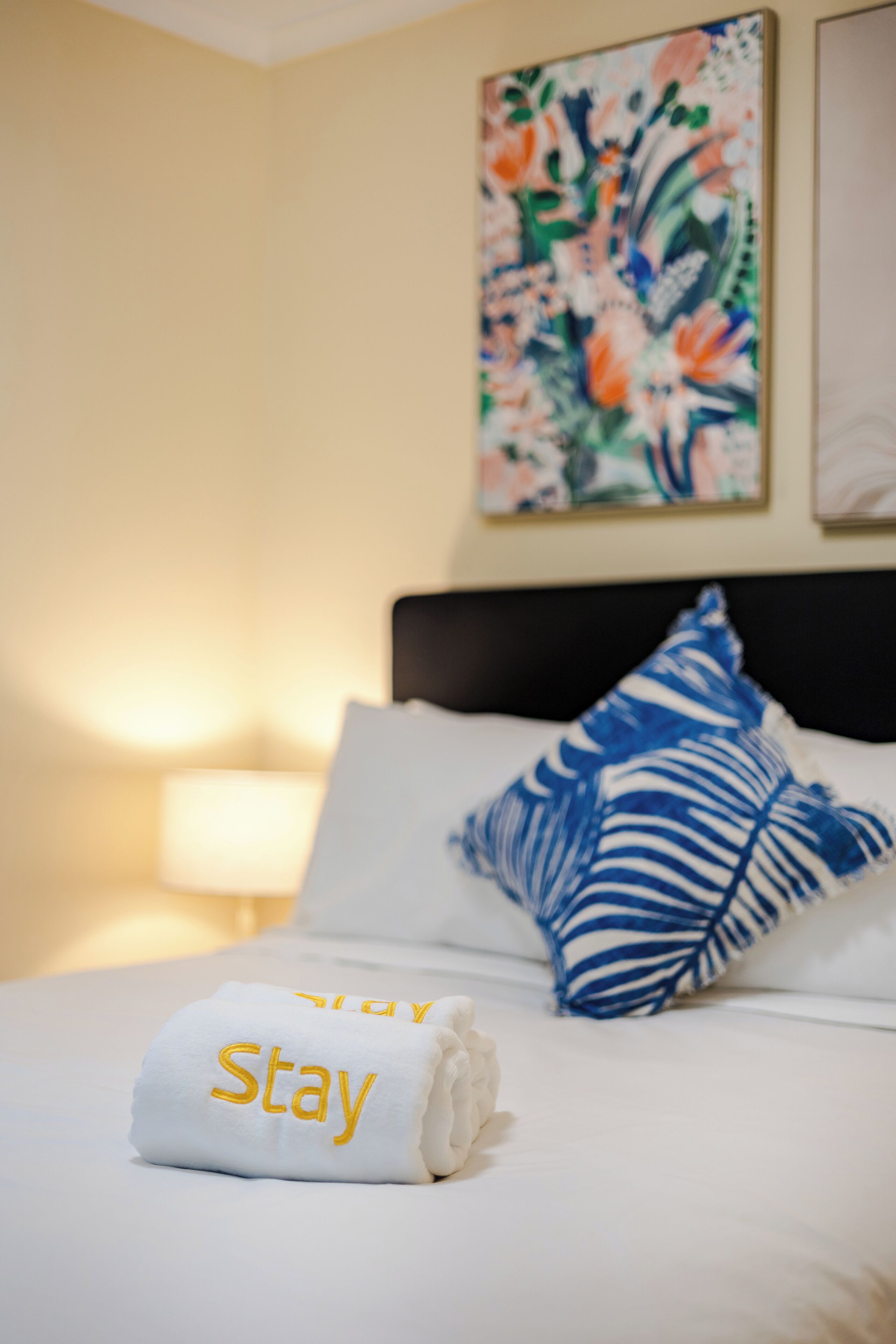 A neatly made bed with a white towel and a pillow with a blue and white leaf pattern.