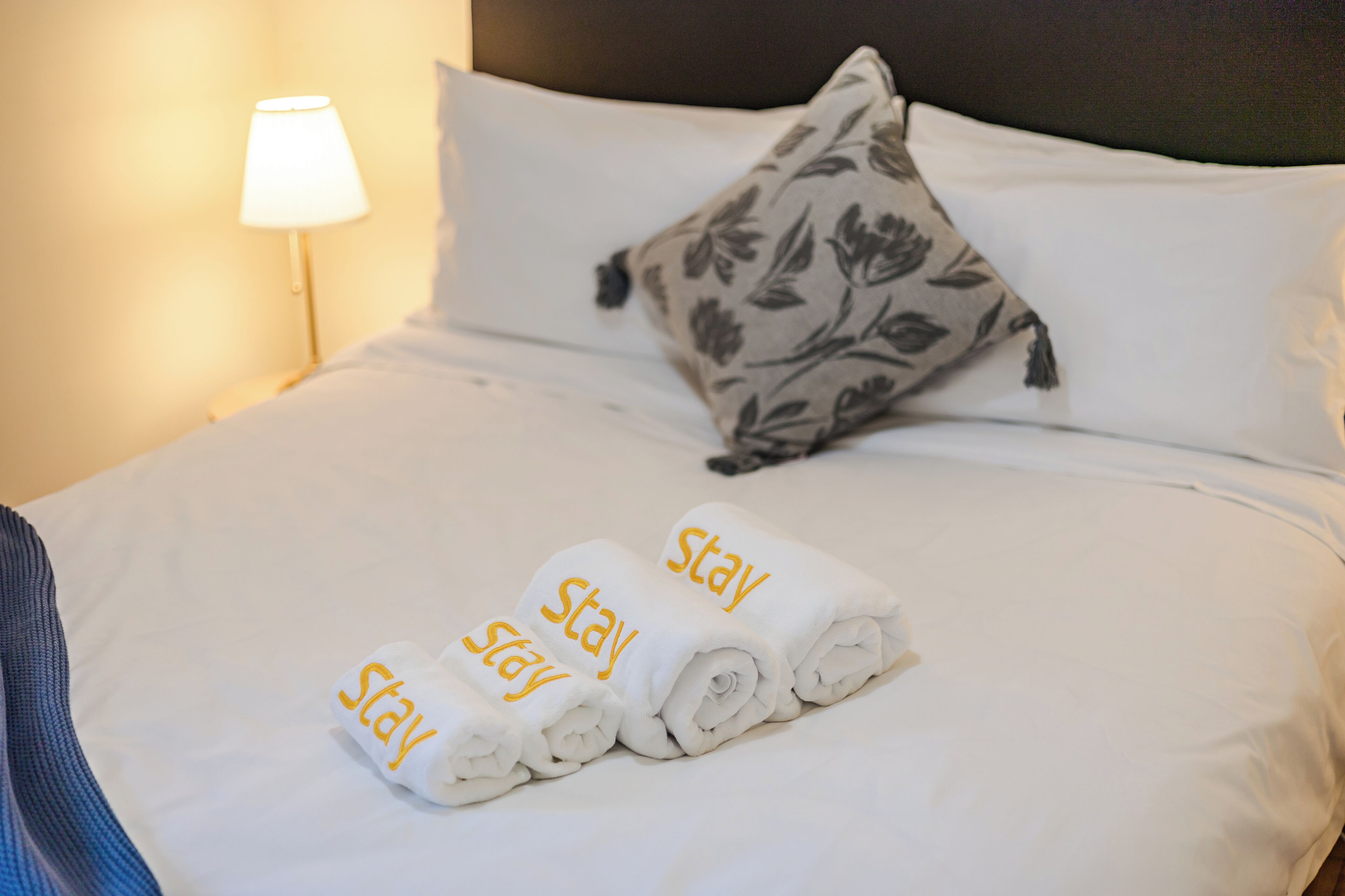 Un lit bien fait, avec des serviettes pliées et un oreiller orné d’un motif floral.