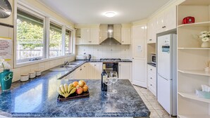 A modern kitchen with a marble countertop, stainless steel appliances, and a view of greenery outside. - StayAU Cozy Family Comfort 5BRM Glen (Glen Waverley)