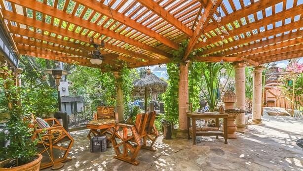 A covered outdoor area with wooden furniture, stone flooring, and lush greenery. - 3 bedroom cottage, peaceful and private, with pool, fitness, flowers and nature (Buda)