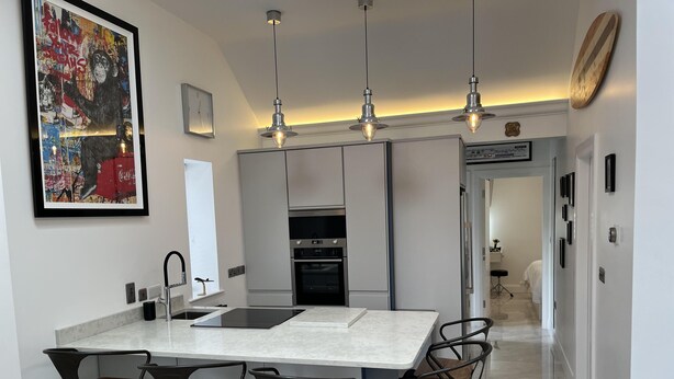 Een moderne keuken met een centraal eiland, barstoelen, hanglampen en een groot kunstwerk in een lijst.