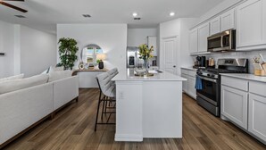 A modern kitchen with white cabinetry, a central island, and a dining area with a sofa and chairs.