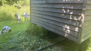 Eine Holzhütte mit geneigtem Dach, umgeben von Gras und einigen Stühlen.