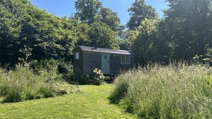 Eine rustikale Holzhütte, umgeben von hohem Gras und Bäumen.