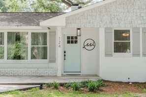 A white house with a light blue door, a number '124' on the wall, and a circular logo above the door.
