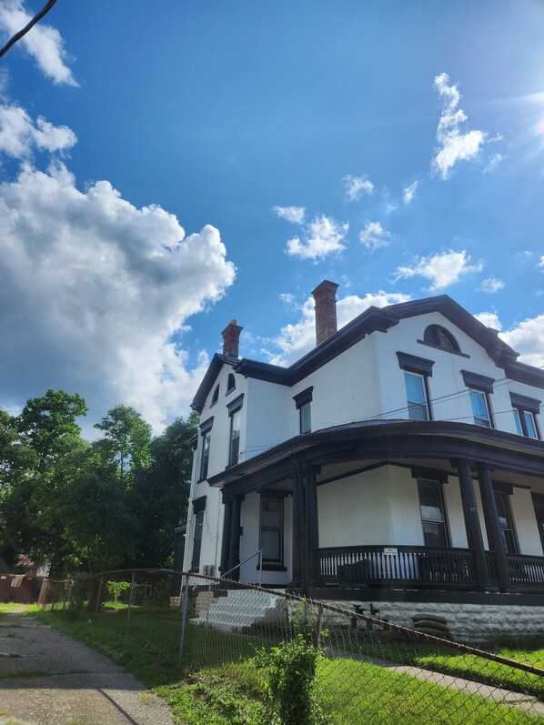 A two-story building with a white facade and black trim, featuring a prominent chimney and a balcony. - Comfortable 8-bdrm, 3-bath with off street parking, near XU, UC, OTR & Downtown (Cincinnati)