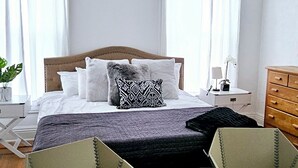 Une chambre à coucher comprenant un lit, deux chaises, un petit tabouret, une table de chevet et une commode.