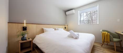 A bedroom with a large bed, a bedside table with a plant, a chair, and a window with a view of trees.