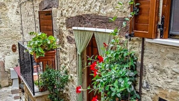 A narrow stone alley with a wooden door, potted plants, and a small balcony with a metal railing. - At the Oven Door (Roccascalegna)