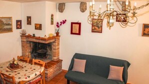 A cozy room with a brick fireplace, a dining table with chairs, a green sofa, and a chandelier. - At the Oven Door (Roccascalegna)