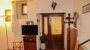 A living room with a television on a wooden cabinet, a small wooden stool, a radiator, and a door with curtains. - At the Oven Door (Roccascalegna)
