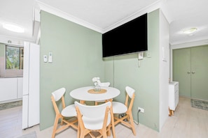 A compact living space with a dining area, a flat-screen TV mounted on the wall, and a kitchenette.