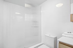 A modern bathroom with a glass shower enclosure, a white toilet, and a wooden vanity with a white countertop.