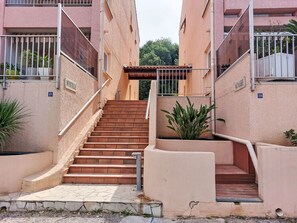 Un conjunto de escalones exteriores que conducen a la entrada de un edificio, con barandilla de metal y plantas en macetas.