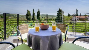 Un balcon avec une table dressée pour deux personnes, offrant une vue panoramique sur un paysage verdoyant, avec des arbres et un bâtiment situé au loin.