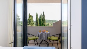 Un balcon avec une table et des chaises, un lit et une vue sur les arbres et les collines.