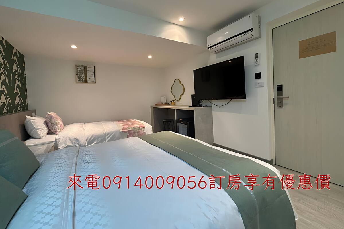 Quarto de hotel moderno com duas camas, uma TV de tela plana, aparelho de ar condicionado e uma porta com placa.