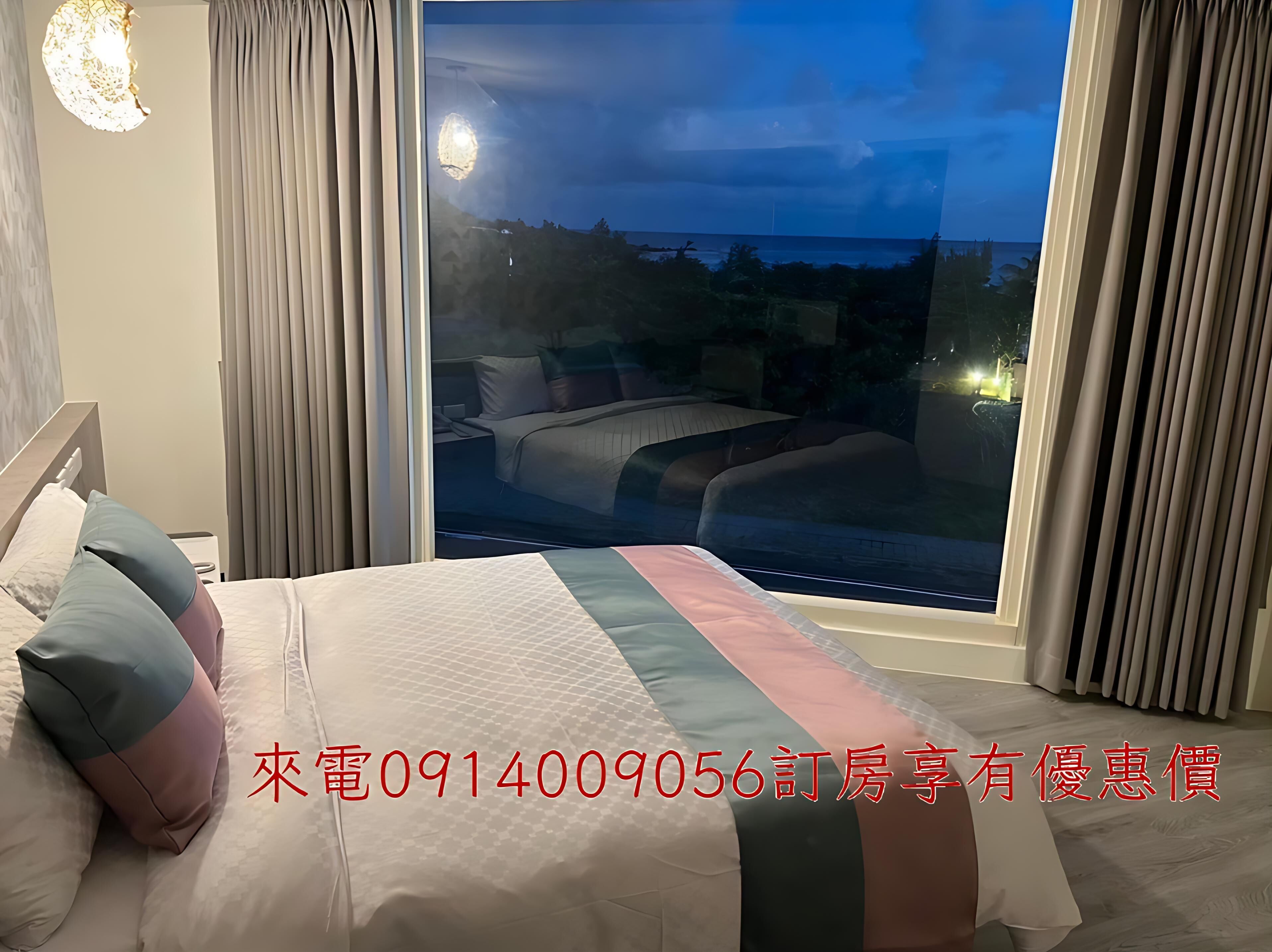 A hotel room with a large bed, a view of the sea, and a contact number for booking.