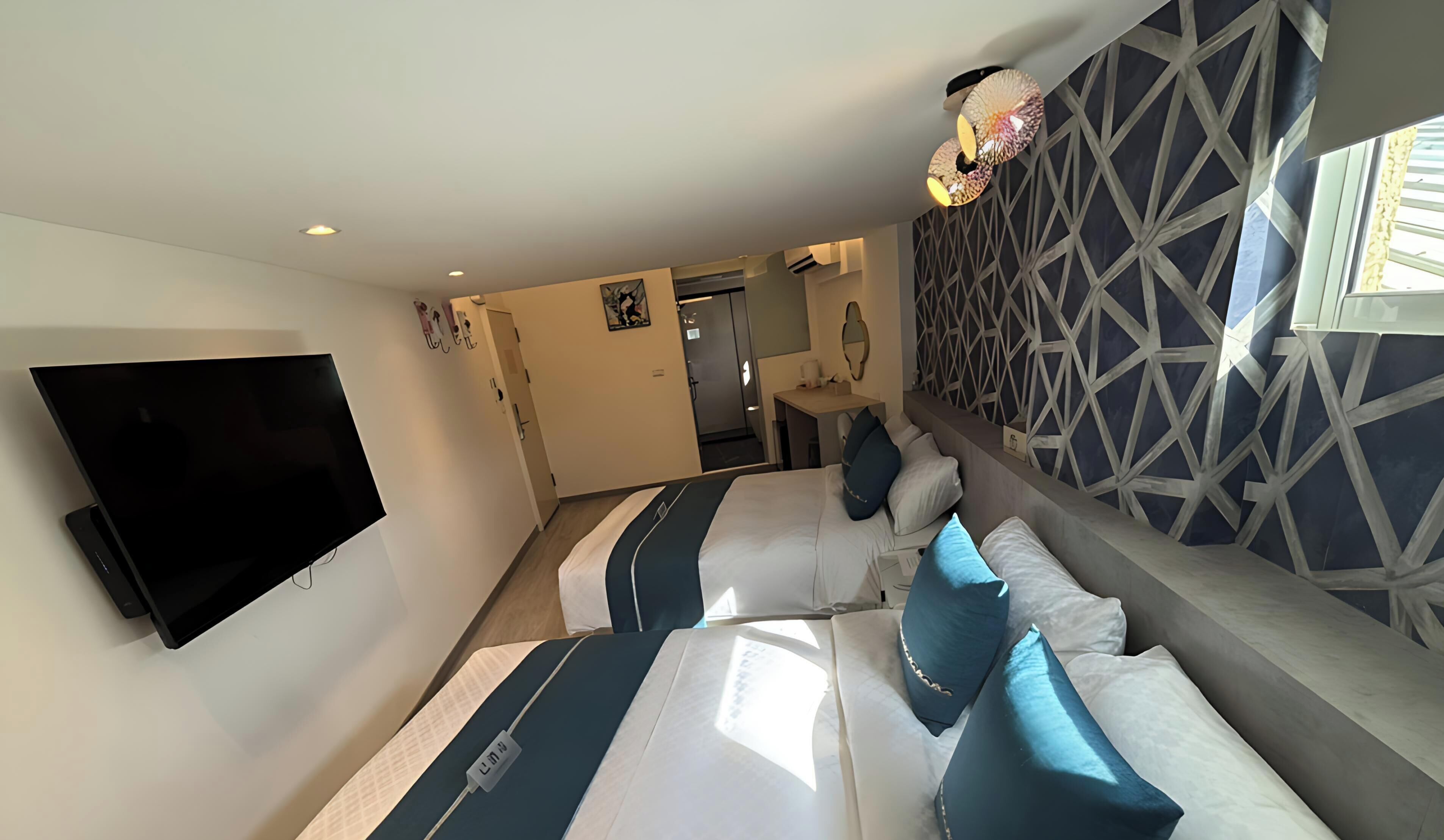 A hotel room with a large flat-screen TV, a sofa bed, a small table, and a decorative wall with geometric patterns.