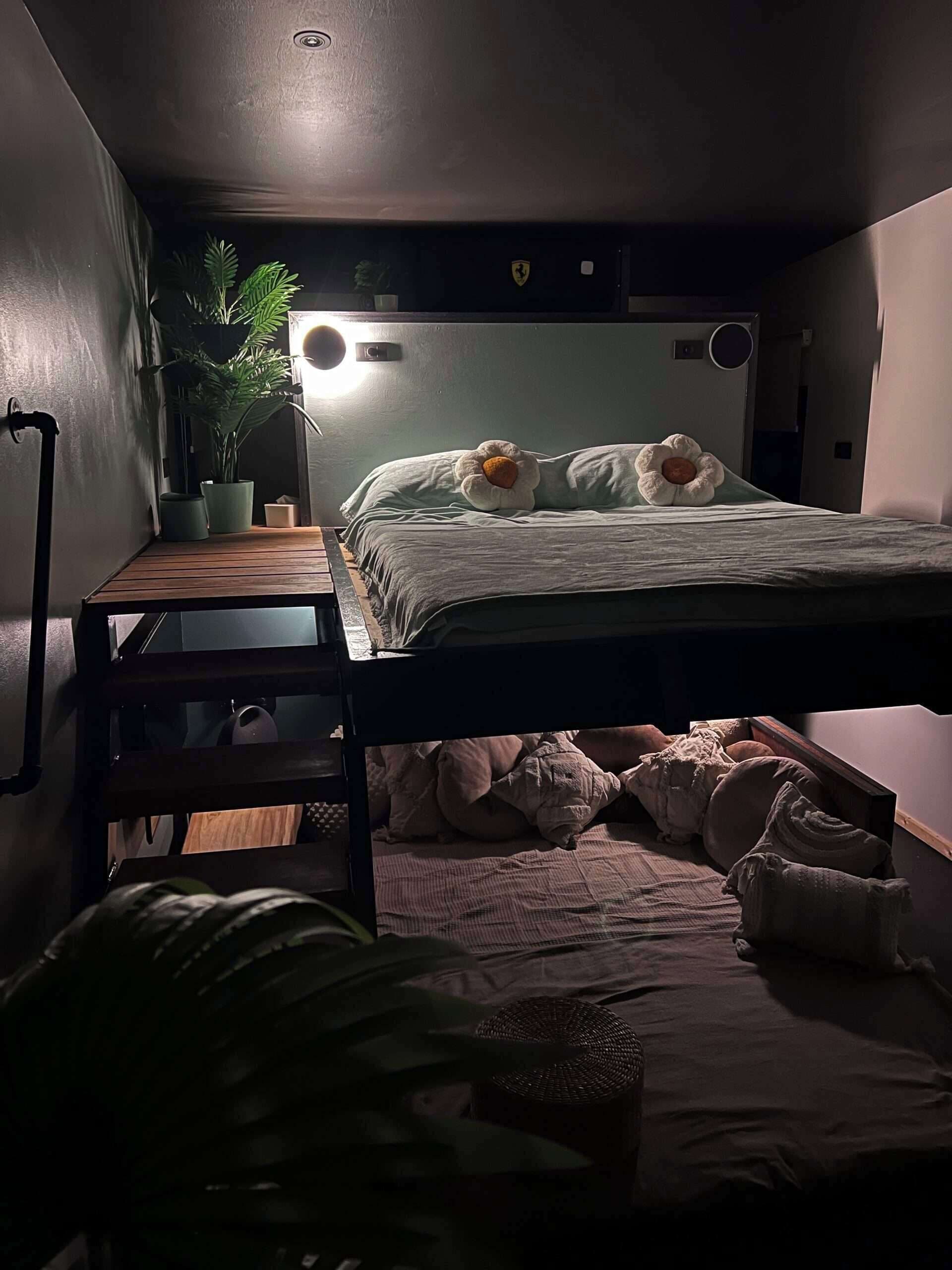 Ein kleines Zimmer mit Etagenbett, Tisch, Blumentopf und Lampe.
