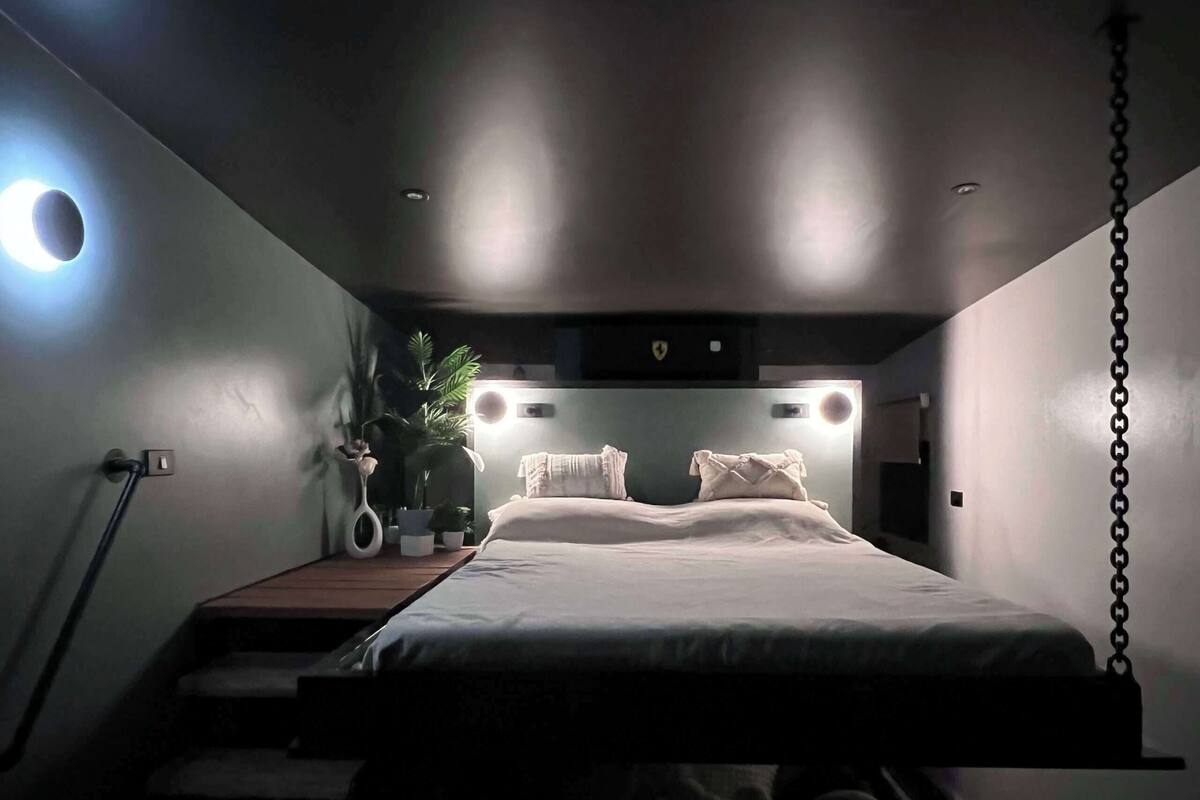 A modern bedroom with a bed, bedside tables, a plant, and a hanging light fixture.