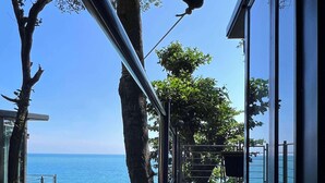 Une terrasse en bois avec des garde-corps en métal, donnant sur une étendue d’eau, avec des arbres et un bâtiment en arrière-plan.