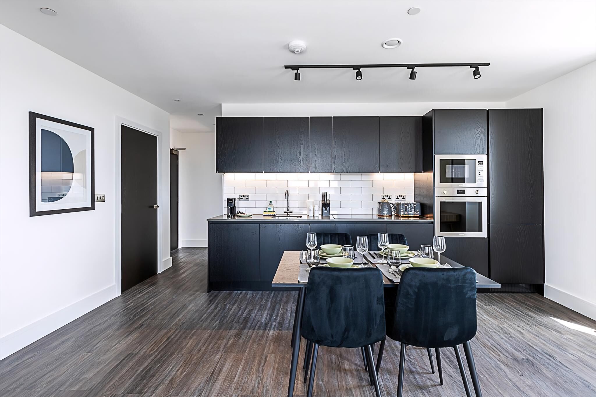 A modern kitchen with dark cabinetry, a central island, and a dining area with a wooden table and chairs.