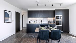 Een moderne keuken met donkere kastjes, een centraal eiland en een eethoek met een houten tafel en stoelen.