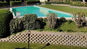 Una piscina rodeada de follaje, con edificios al fondo y un cielo despejado.