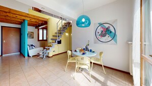 Amplia sala de estar con una escalera, una mesa de comedor con sillas y una obra de arte colgada en la pared.
