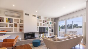 Una sala de estar moderna con chimenea, televisor y un ventanal que ofrece vistas al exterior.