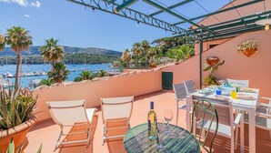 Terraço com mesa posta para refeições, com vista para uma marina com barcos e paisagem costeira.
