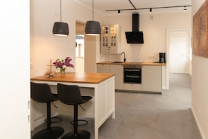 Une cuisine moderne avec un îlot central en bois, deux tabourets de bar, des luminaires suspendus et un four encastré.