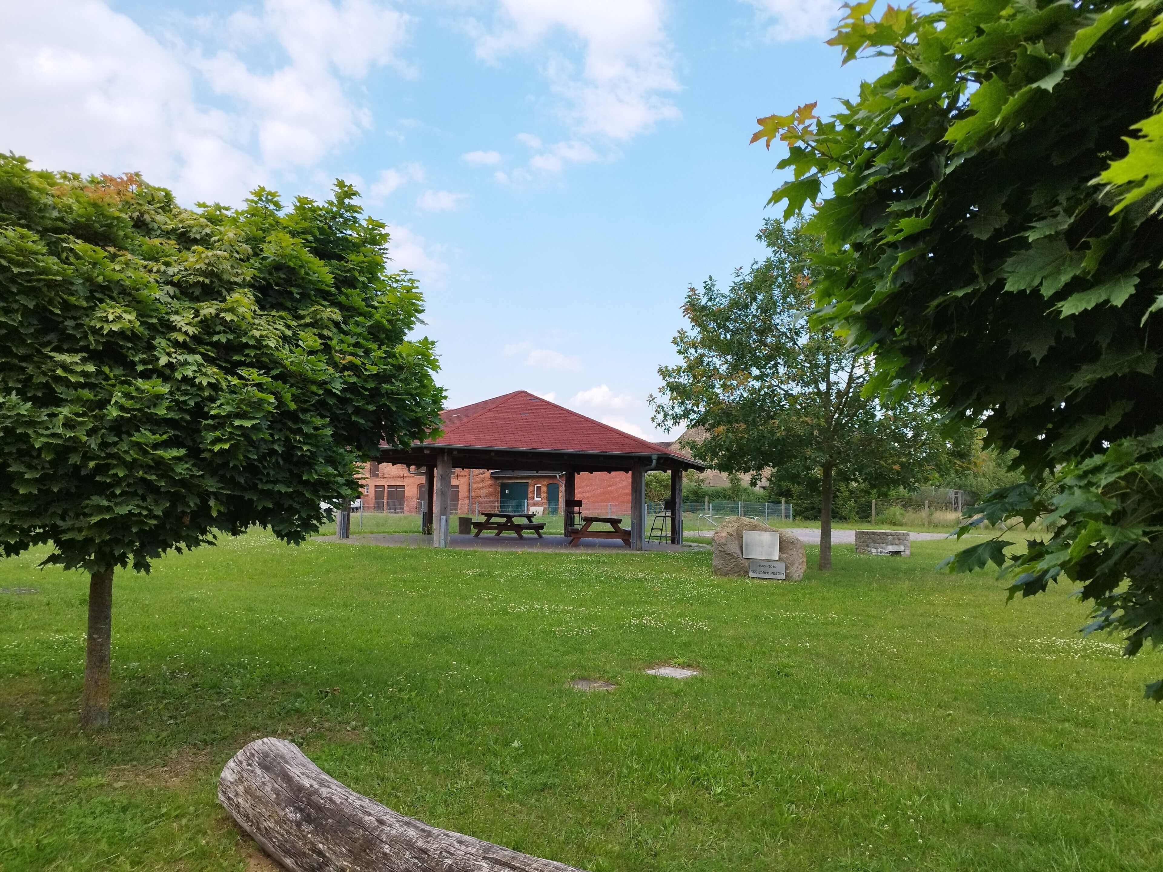 En park med en paviljong, picknickbord och ett stort träd.