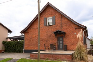 Une maison en briques avec un porche à l’avant, une porte et une fenêtre avec des volets.