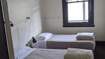 Een kamer met twee bedden, een raam met zonwering, een hanglamp en een zichtbaar stopcontact.