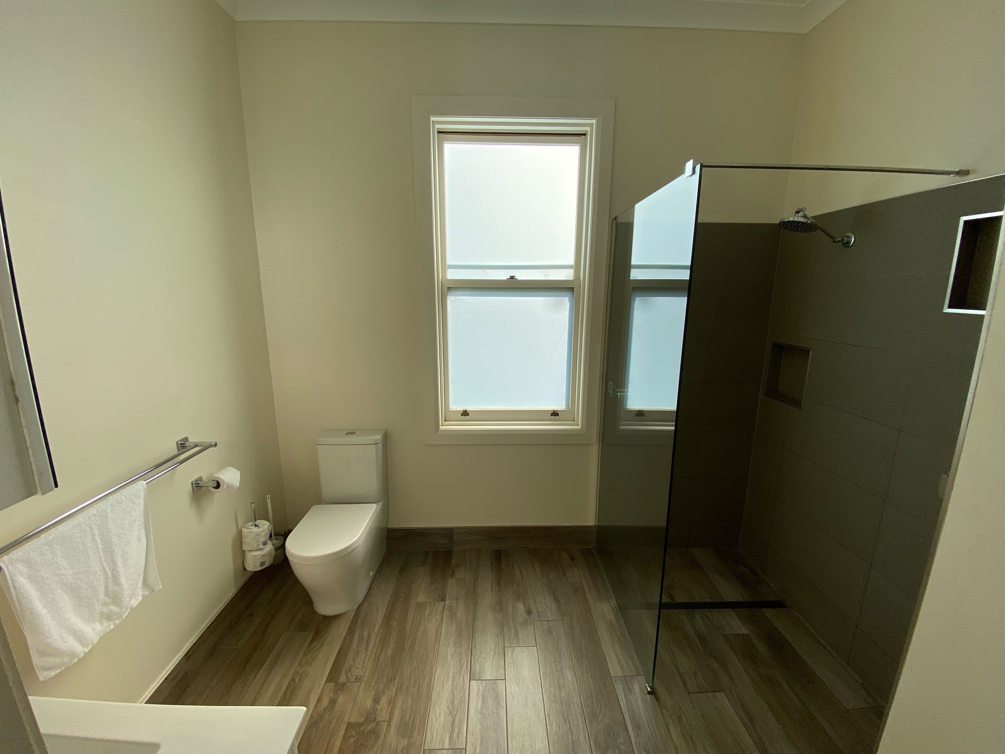 A bathroom with a toilet, a window, a shower area, and a towel rack.