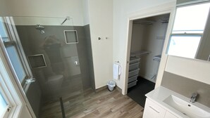 Een moderne badkamer met een douchecabine van glas, een wit wastafelmeubel en een inloopkast met planken.