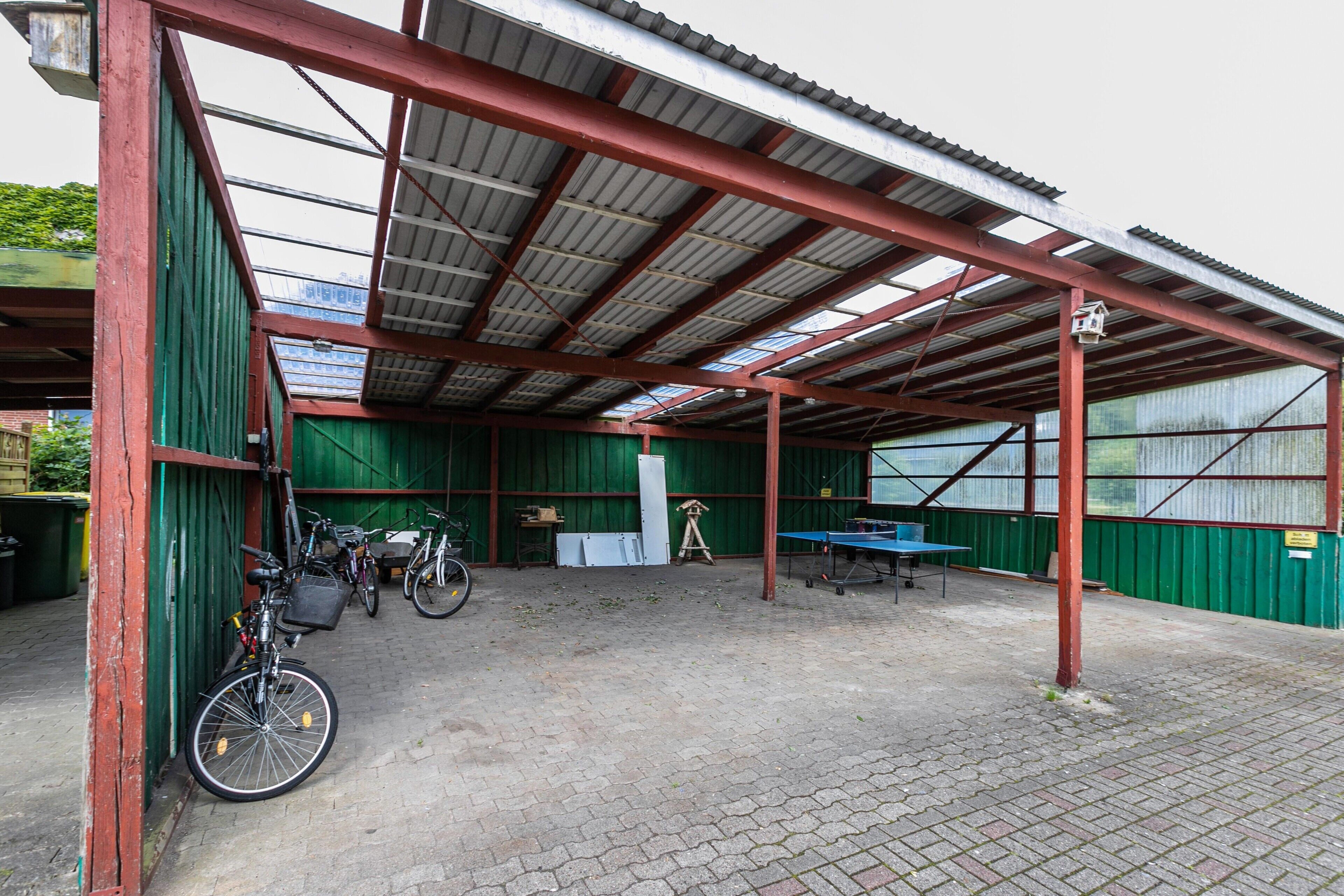 A covered outdoor area with bicycles, a ping pong table, and a green building structure.