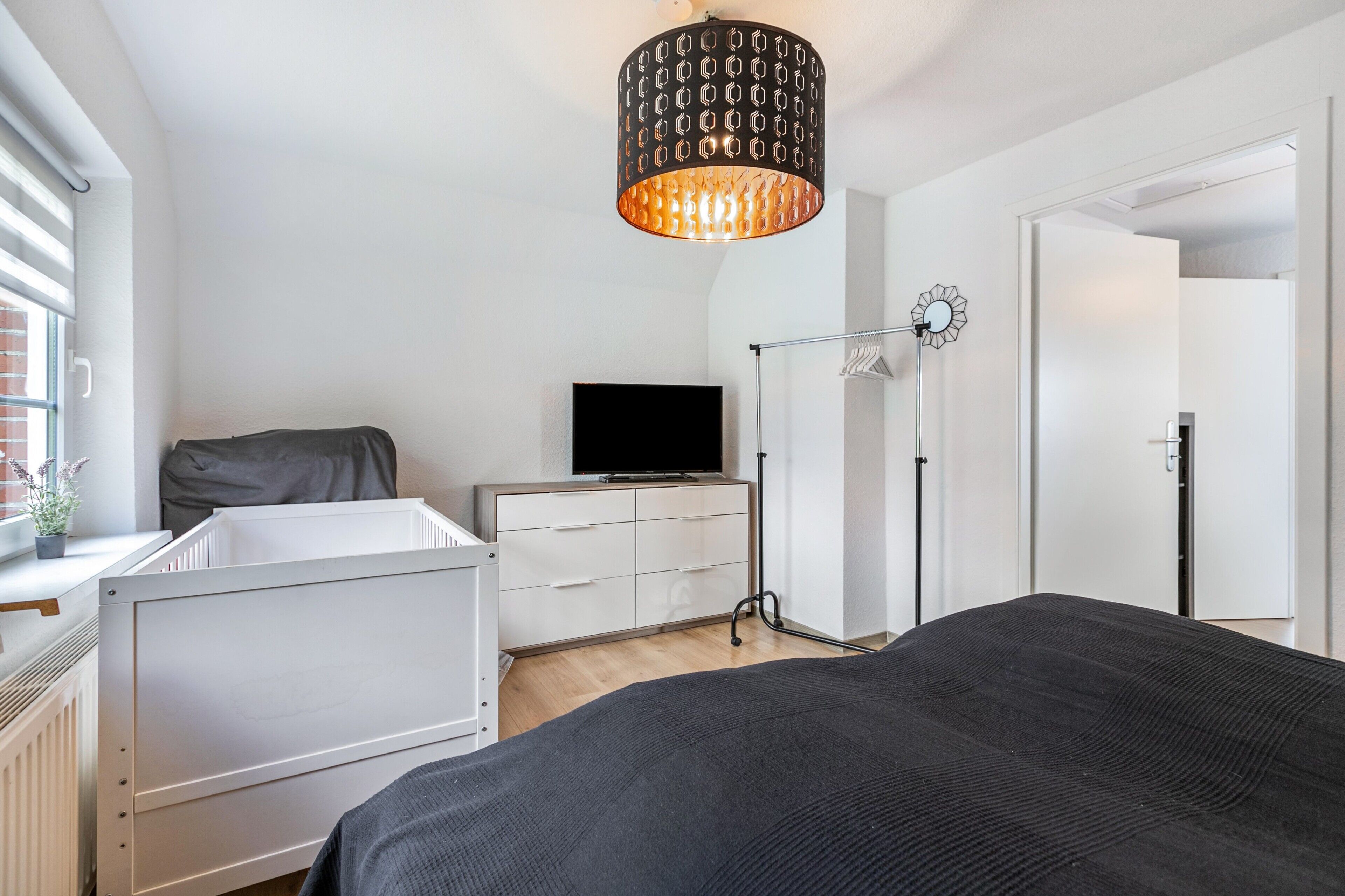 Ett sovrum med en säng, en byrå, en tv, en garderob och en hängande lampa.