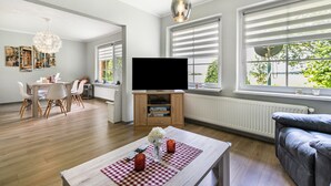 Een moderne woonkamer met een flatscreen-tv, eethoek en grote ramen.