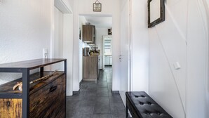 Een gang met een houten bank, een donkerhouten tafel en een keuken op de achtergrond.