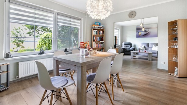Een moderne woonkamer met een eethoek, grote ramen, een boekenkast en een open haard.