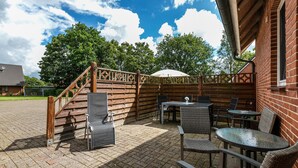 Een terras buiten met rieten meubilair, een overdekte zithoek en een houten omheining.